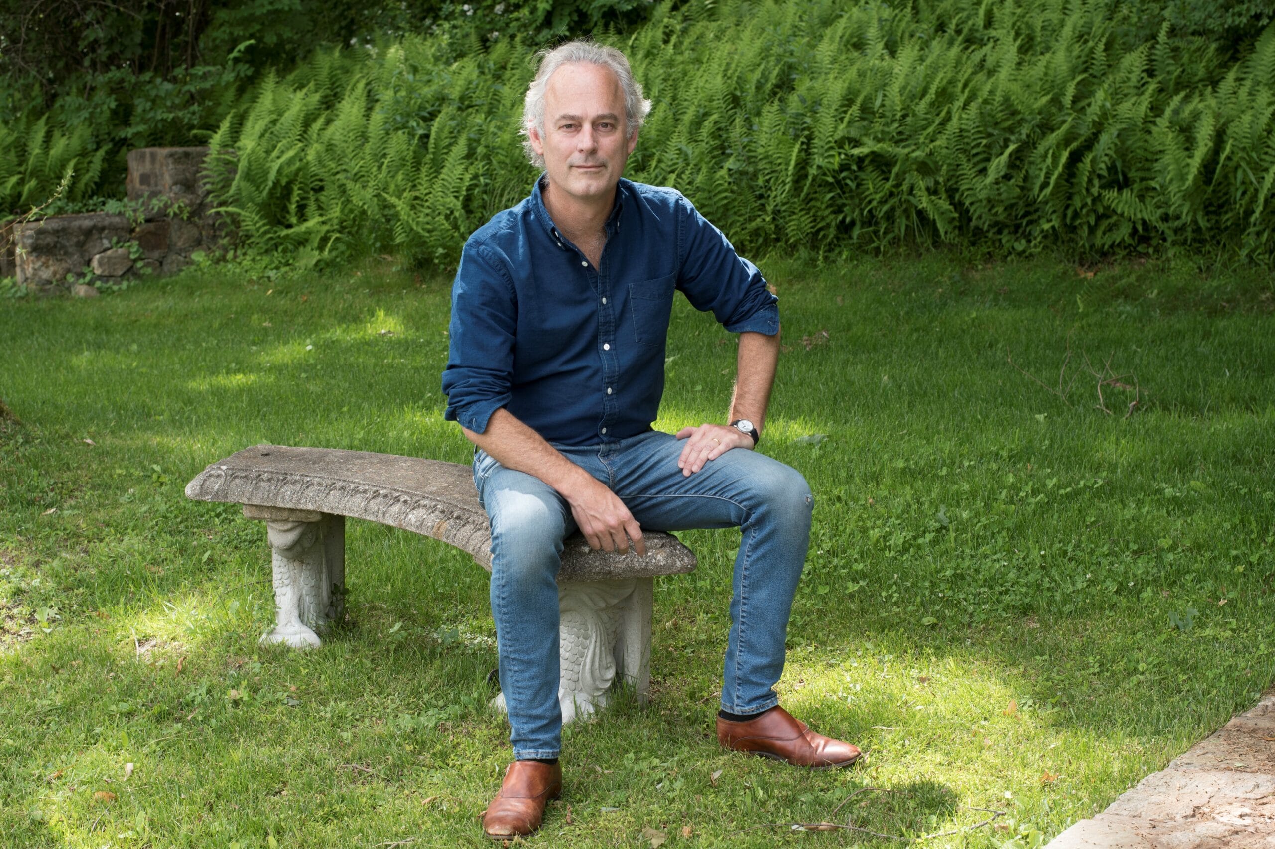 A photo of author Amor Towles sitting on a stone bench.