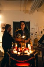 Still from the movie A Kadish for Bernie Madoff. Two people stand around a table filled with lit candles in a small apartment.